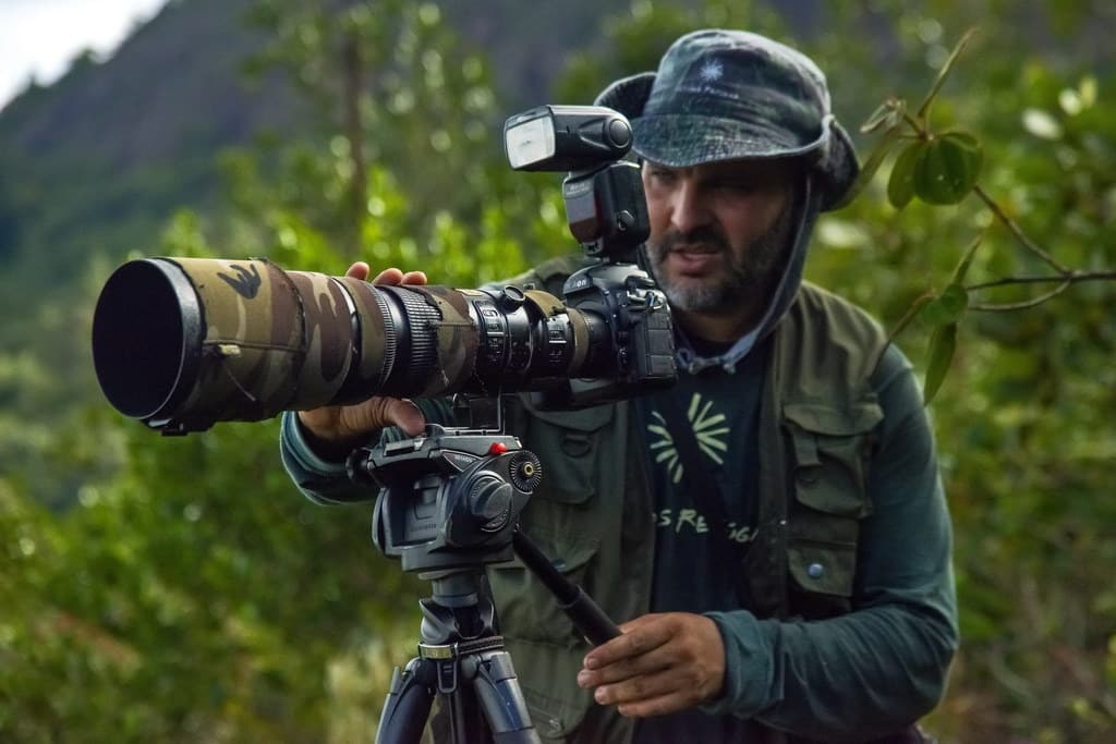 Fotógrafo de natureza usando lente teleobjetiva em um tripé para capturar imagens do ambiente natural.