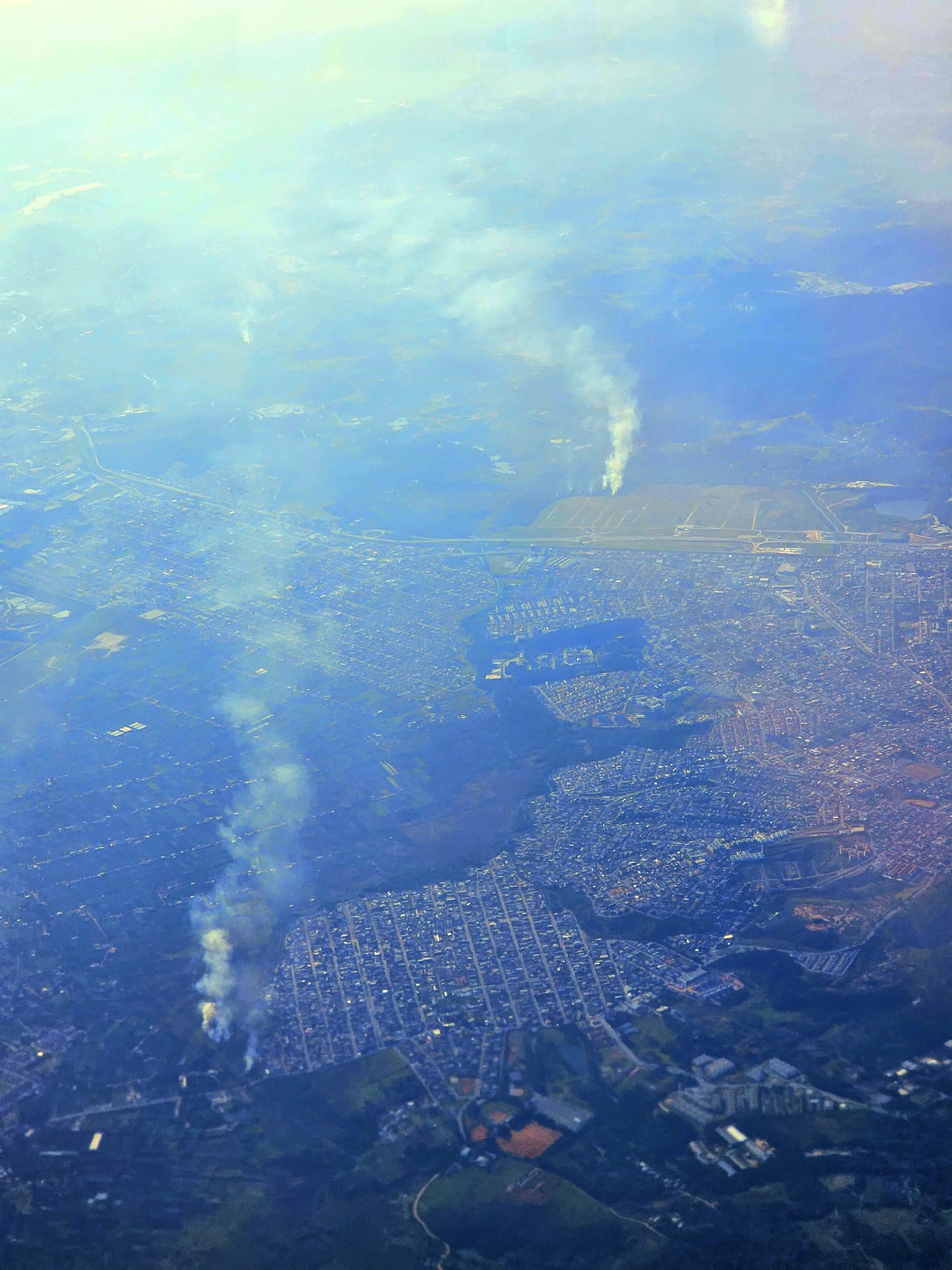 Texto Alternativo:** Fotografia aérea de focos de incêndio e densa camada de fumaça, vista da janela de um avião, durante o voo entre São Paulo e Espírito Santo