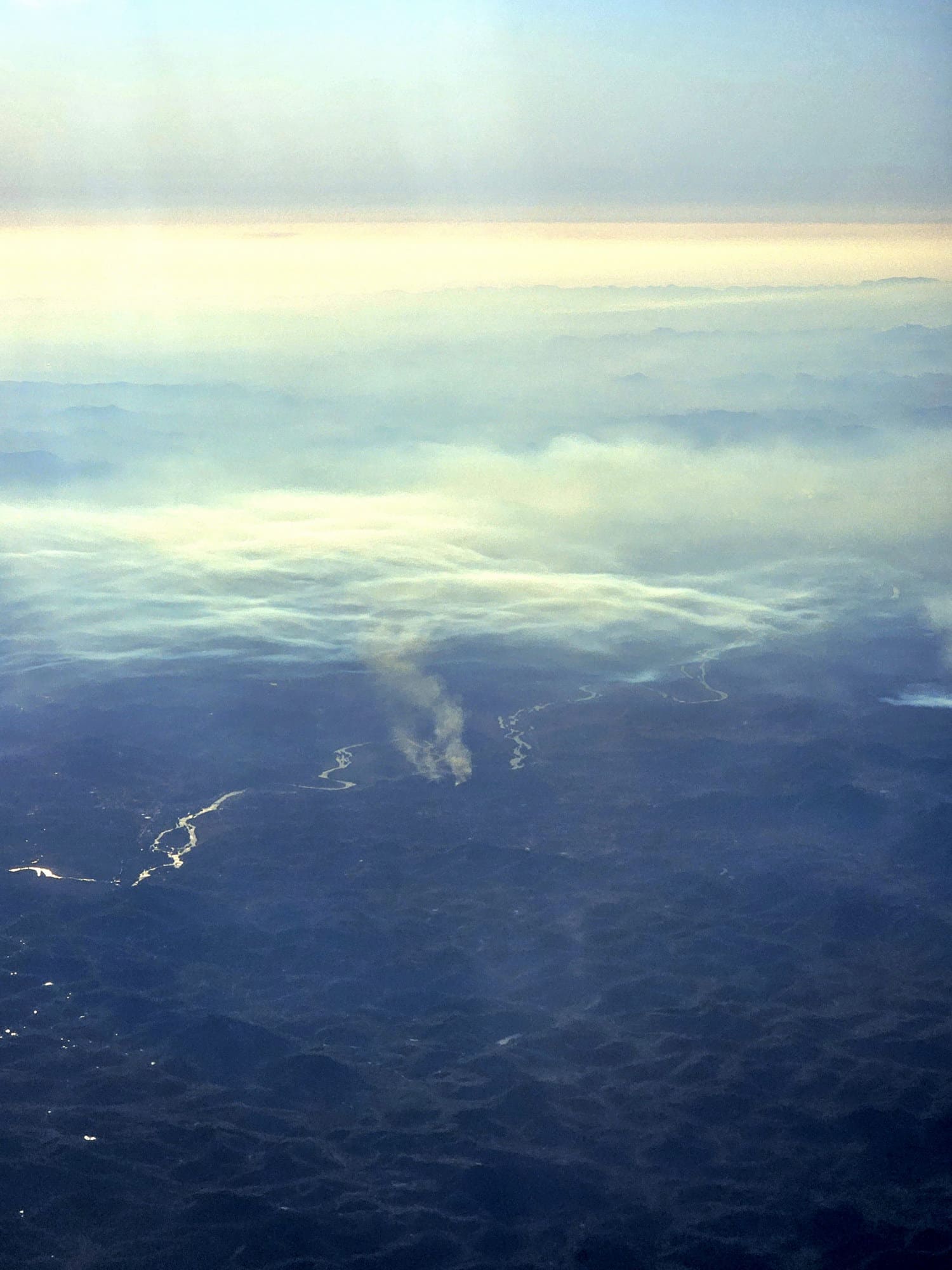 Texto Alternativo:** Fotografia aérea de focos de incêndio e densa camada de fumaça, vista da janela de um avião, durante o voo entre São Paulo e Espírito Santo.